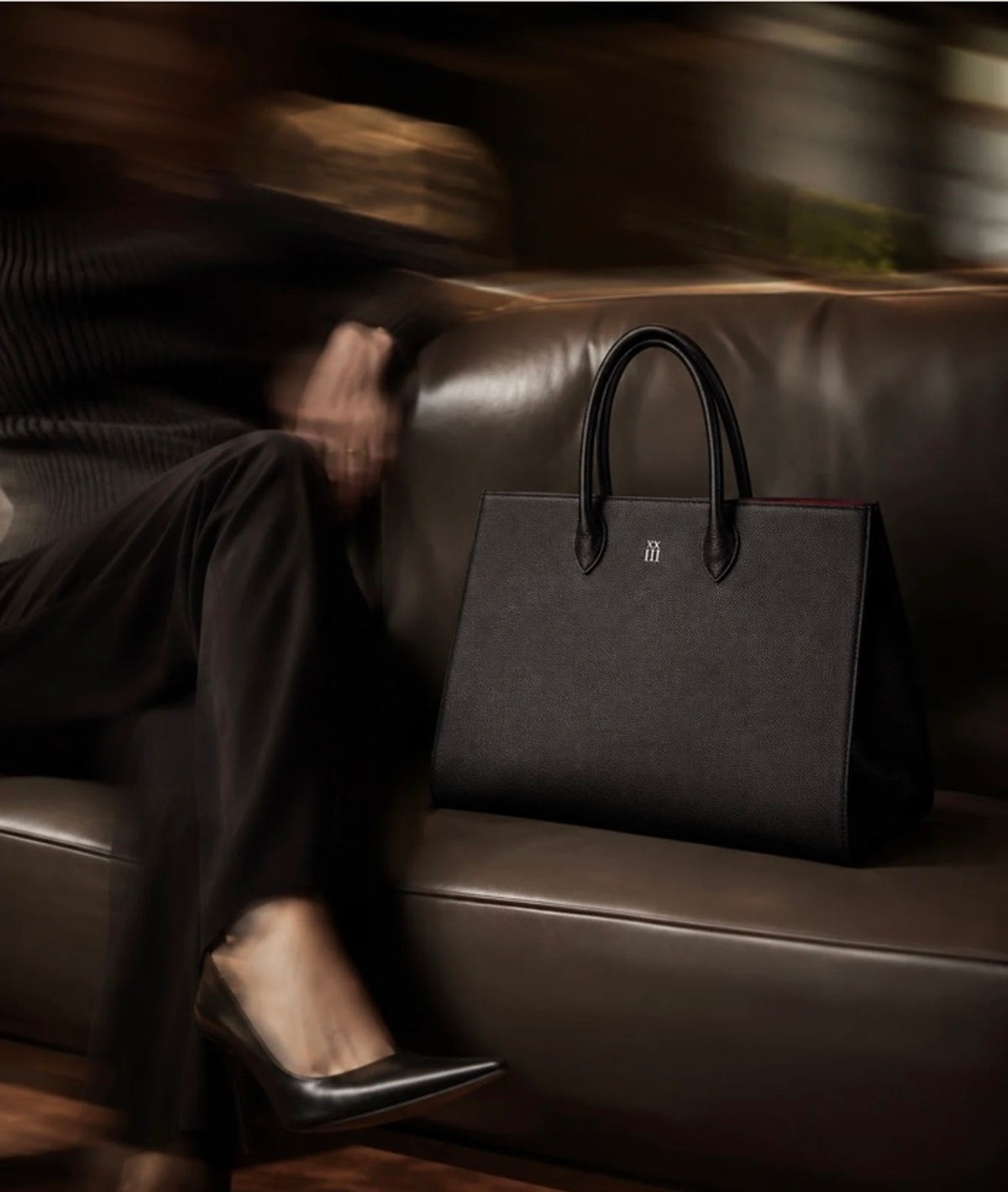 Margaux black pebbled leather tote on a chocolate leather sofa